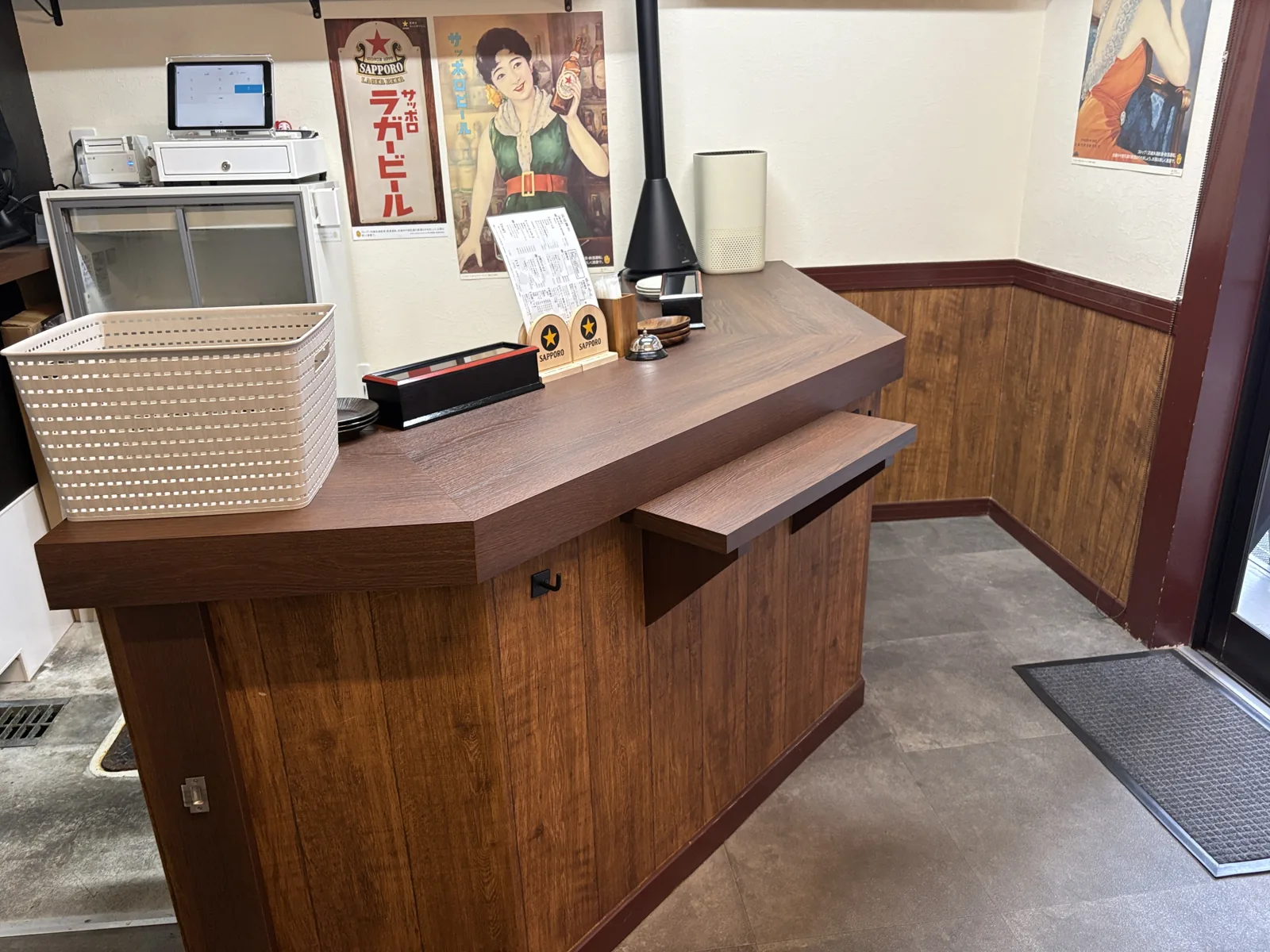 1階の立ち飲みカウンター。木目の天板に赤星の瓶とサッポロのロゴ入りメニュースタンド。奥の壁にサッポロのレトロなポスター