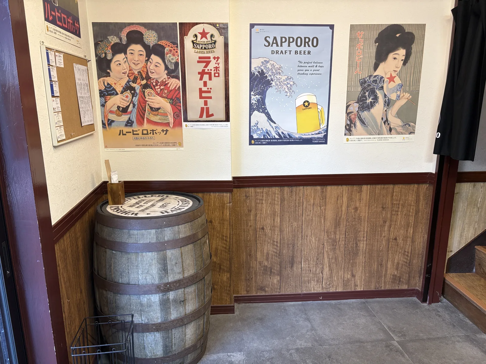 入口脇の角に置かれたウイスキー樽のテーブル。壁にサッポロラガービールやサッポロビールの古いポスターが並ぶ