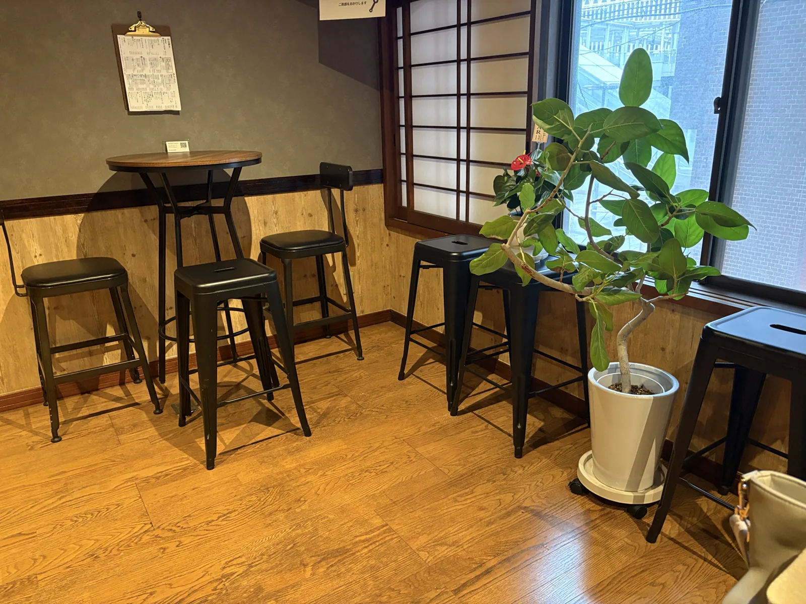 2階の席。丸いハイテーブルに黒いスツールが3脚。窓際に障子と観葉植物