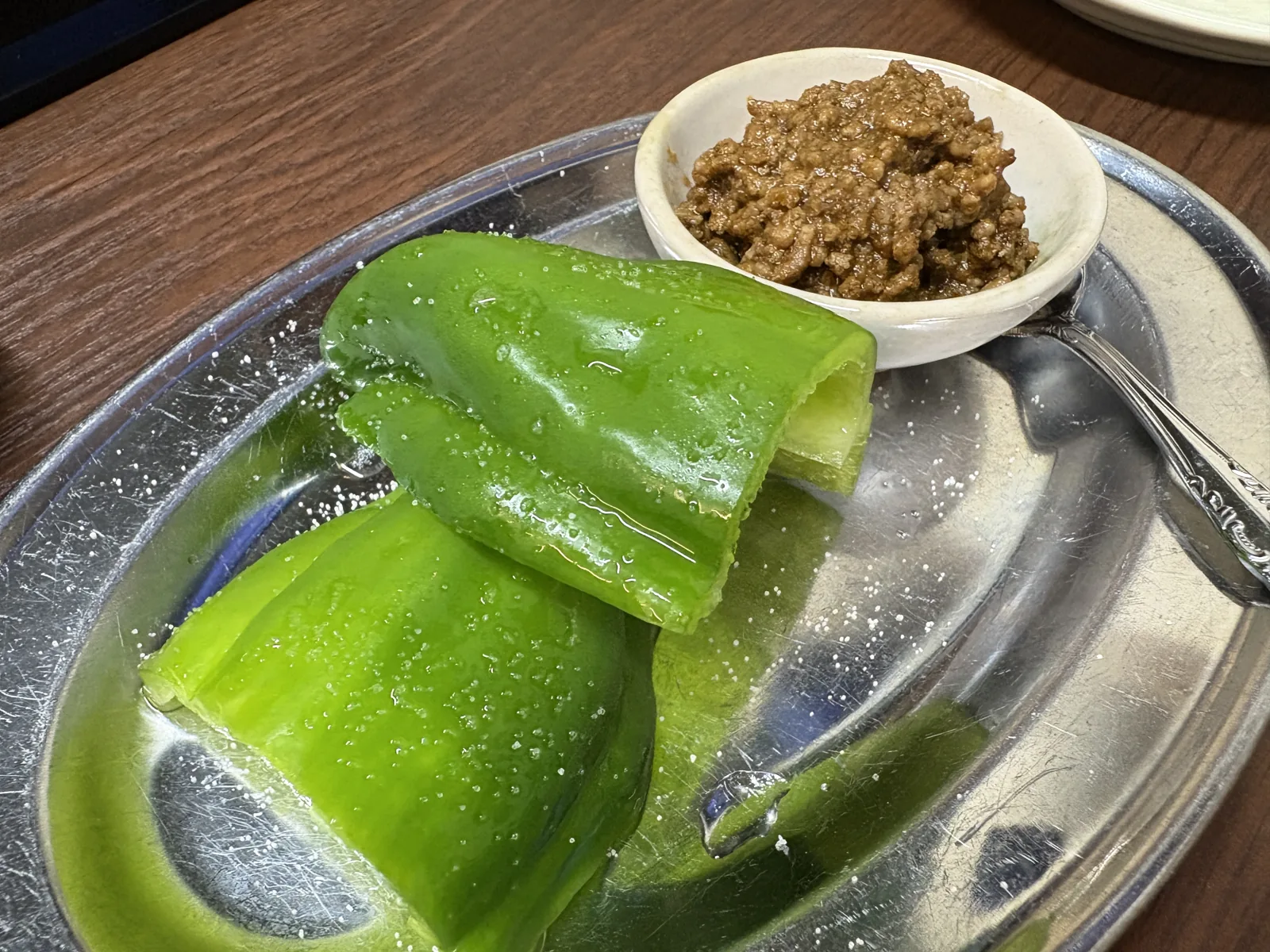 銀の皿に、冷やして水滴のついた生ピーマンが2つ。小皿に肉味噌のようなタコスミート