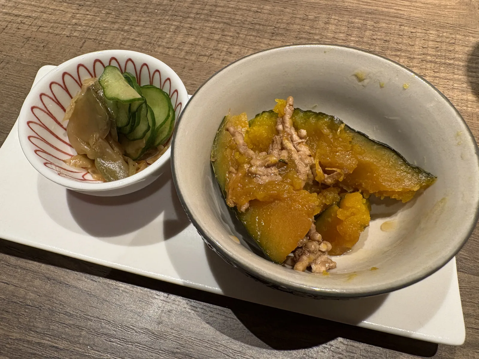 お通しの小鉢2つ。かぼちゃとそぼろの煮物、きゅうりの和え物
