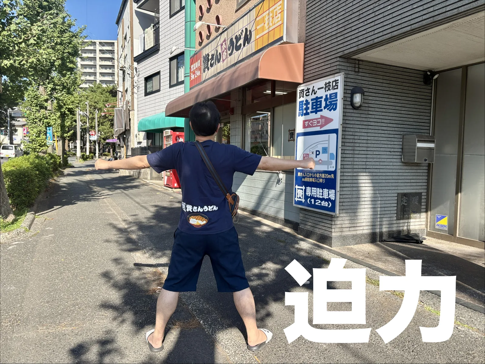 資さんうどん一枝店の前で、資さんうどんTシャツ姿のダイハクリキが両手を広げる後ろ姿。「迫力」の文字入り