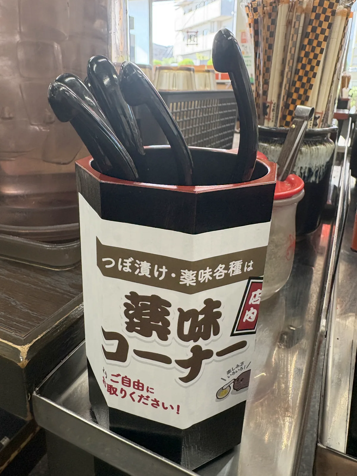 卓上の箸立てに巻かれた「つぼ漬け・薬味各種は店内薬味コーナーよりご自由にお取りください!」の案内