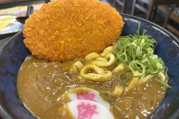 出汁カレーうどんに大判コロッケをのせて。ネギとかまぼこ、カレー色に染まった麺