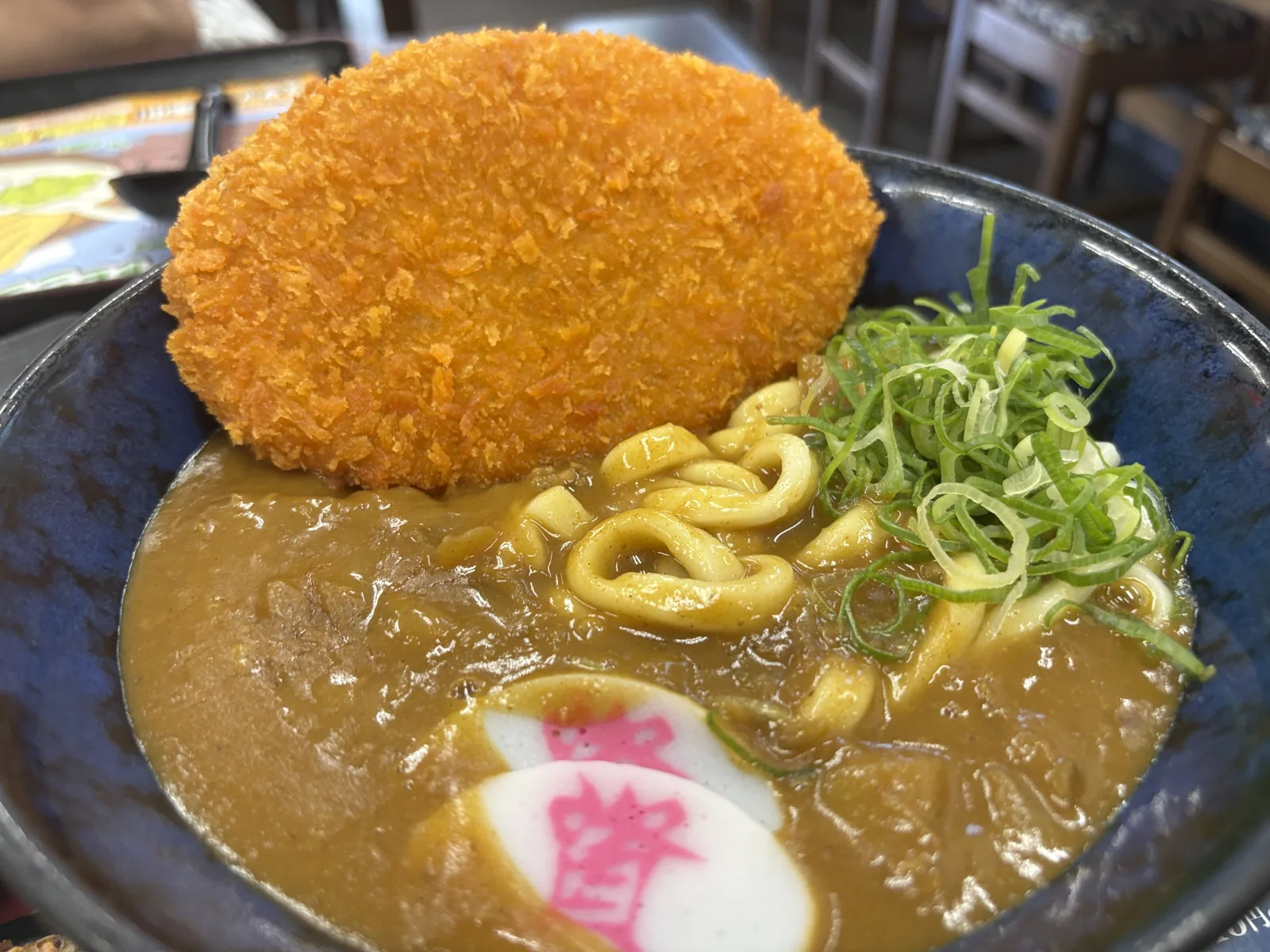 出汁カレーうどんに大判コロッケをのせて。ネギとかまぼこ、カレー色に染まった麺