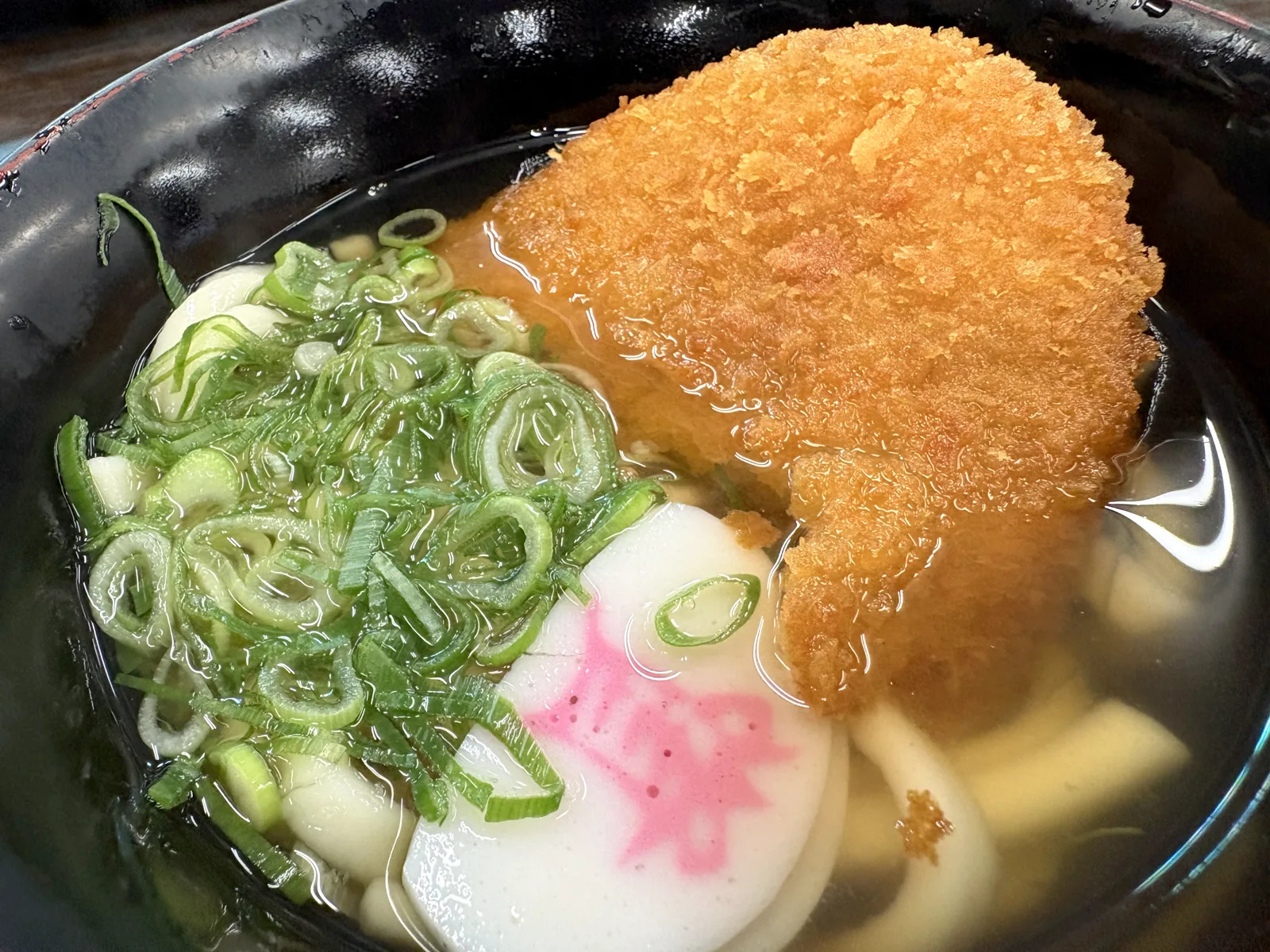 うどんの出汁に浸かった大判コロッケ。ネギとかまぼこの横で衣が出汁を吸っている