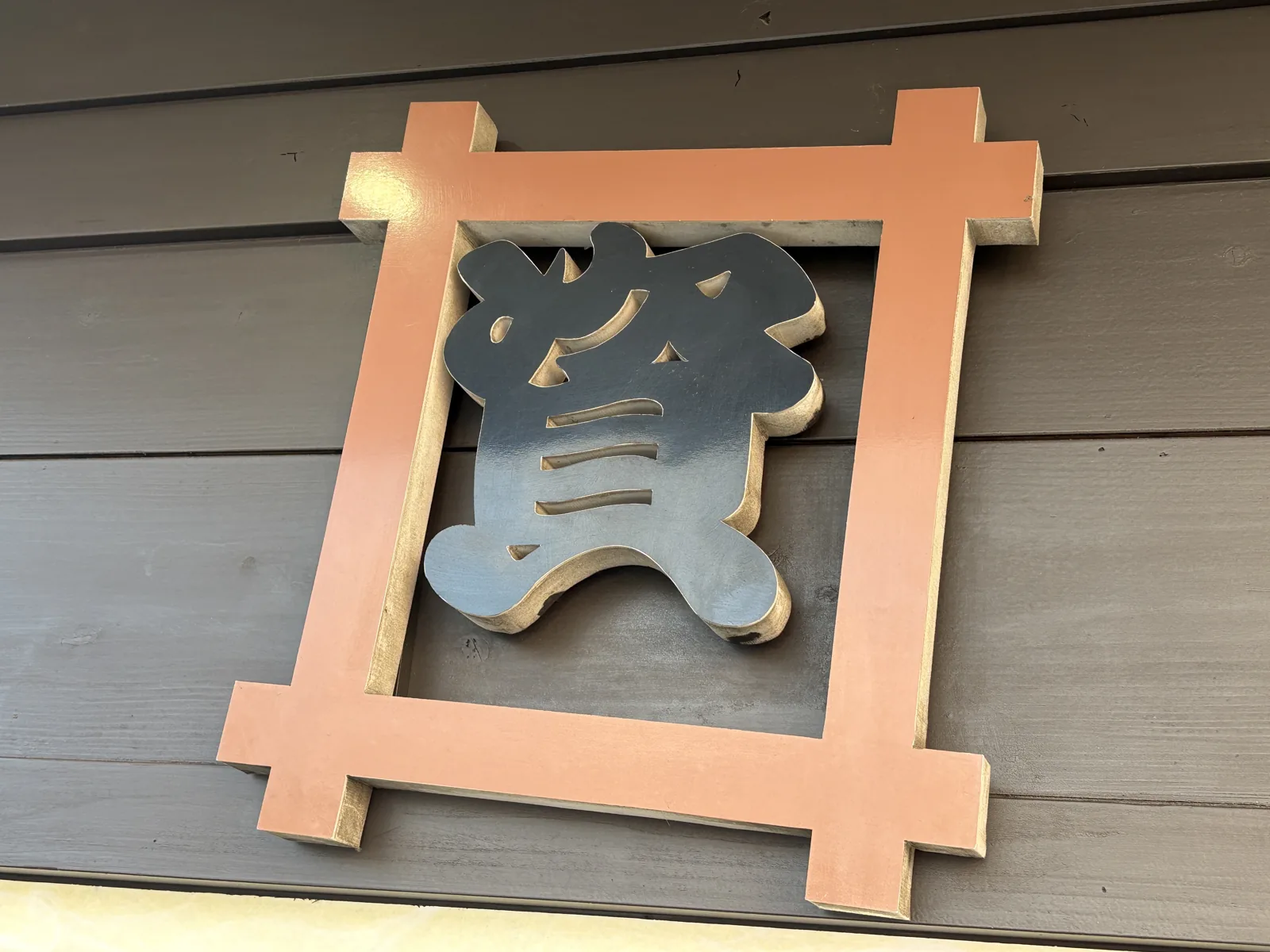 陣山店の外壁に掛かる「資」の看板。枠の中で文字が少し傾いている