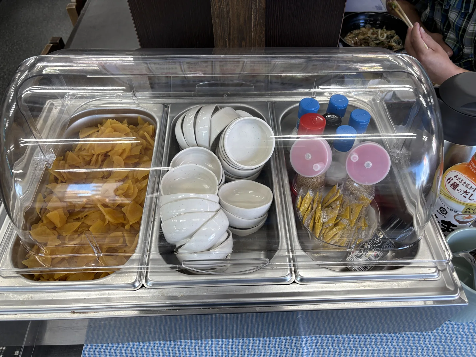 クリアカバーの中につぼ漬け、小皿、調味料が並ぶ薬味コーナーを正面から