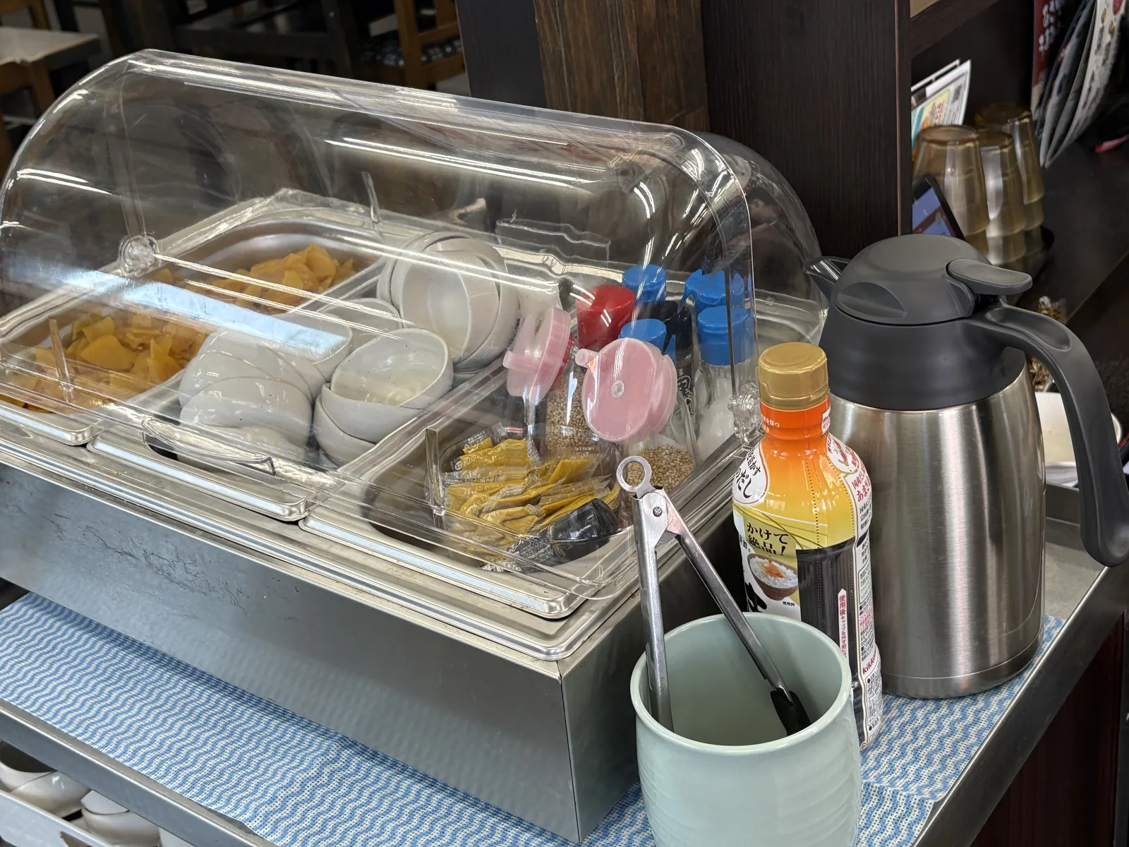 薬味コーナーを斜めから。つぼ漬けと小皿の横に調味料、右手にポットとボトルが並ぶ
