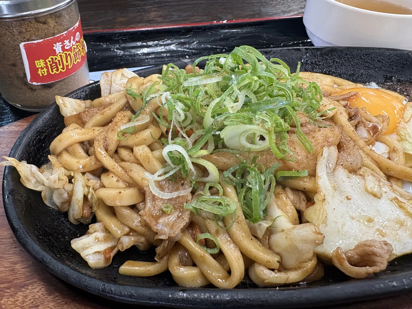 ネギをたっぷりのせた焼きうどんのアップ。奥に削り節粉の容器