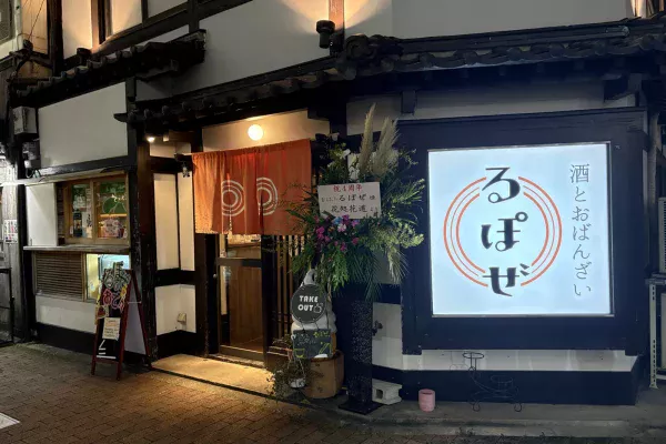 白壁に黒い柱、瓦の庇の古民家。オレンジののれんと「酒とおばんざい るぽぜ」の光る看板