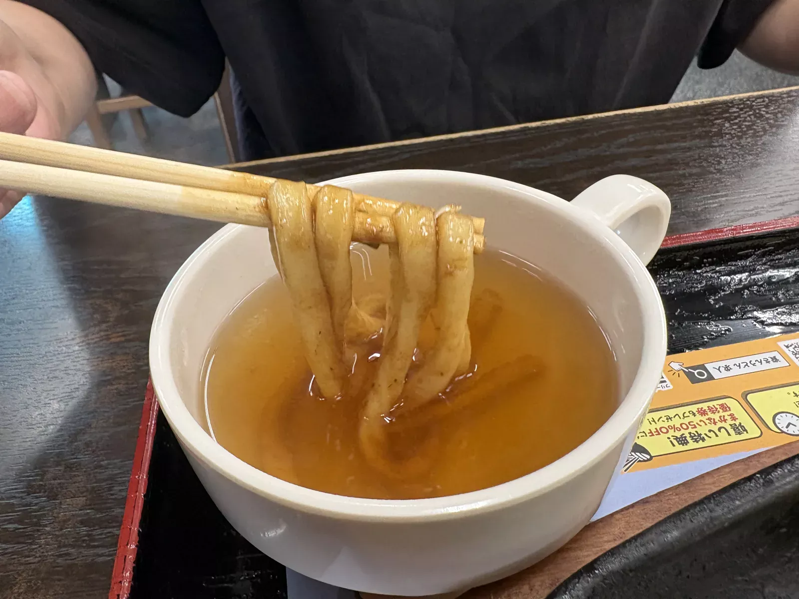 箸で持ち上げた焼きうどんを出汁のカップにくぐらせている