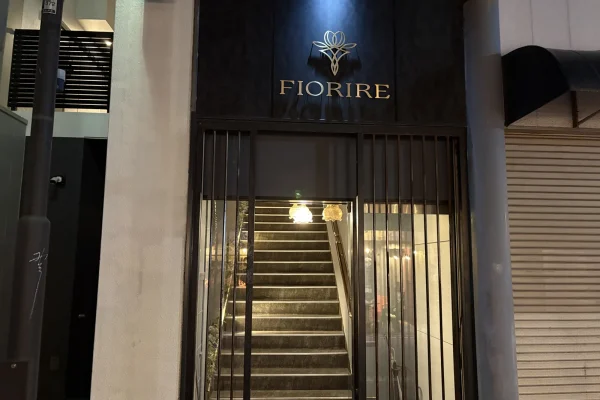 黒い壁に金色の花のロゴと「FIORIRE」の文字。格子の奥にランプに照らされた階段が続く