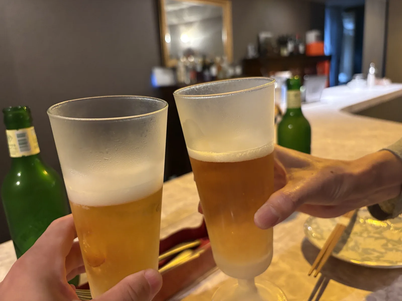瓶のハートランドを注いだグラス2つで乾杯。奥にカウンターと飾り棚