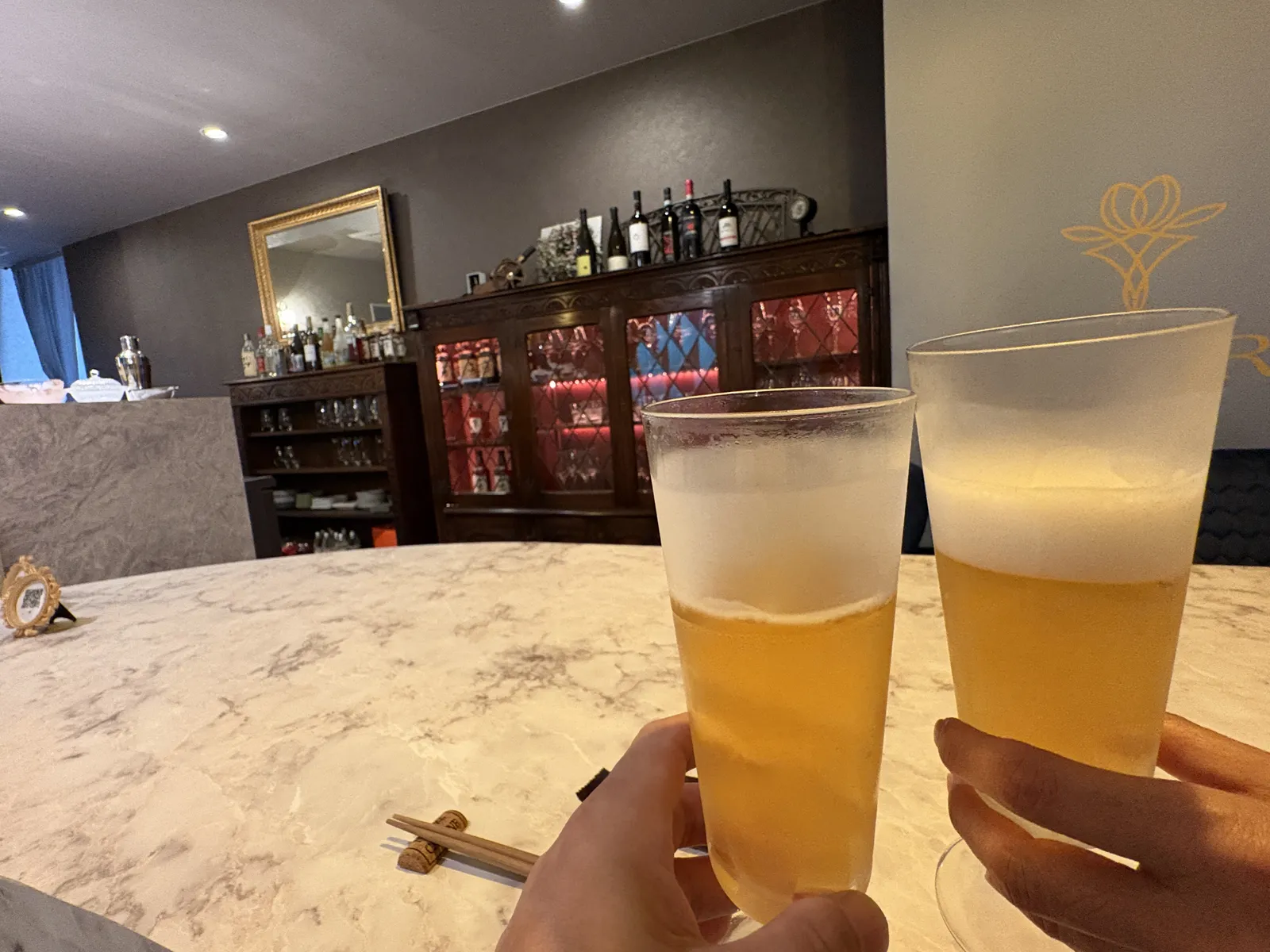 グラスに注いだビールで乾杯。奥に赤いガラス扉の棚