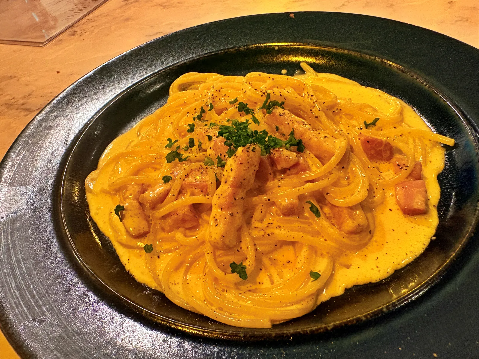 黒い皿に盛られたクリームパスタ。ベーコンとパセリがのる