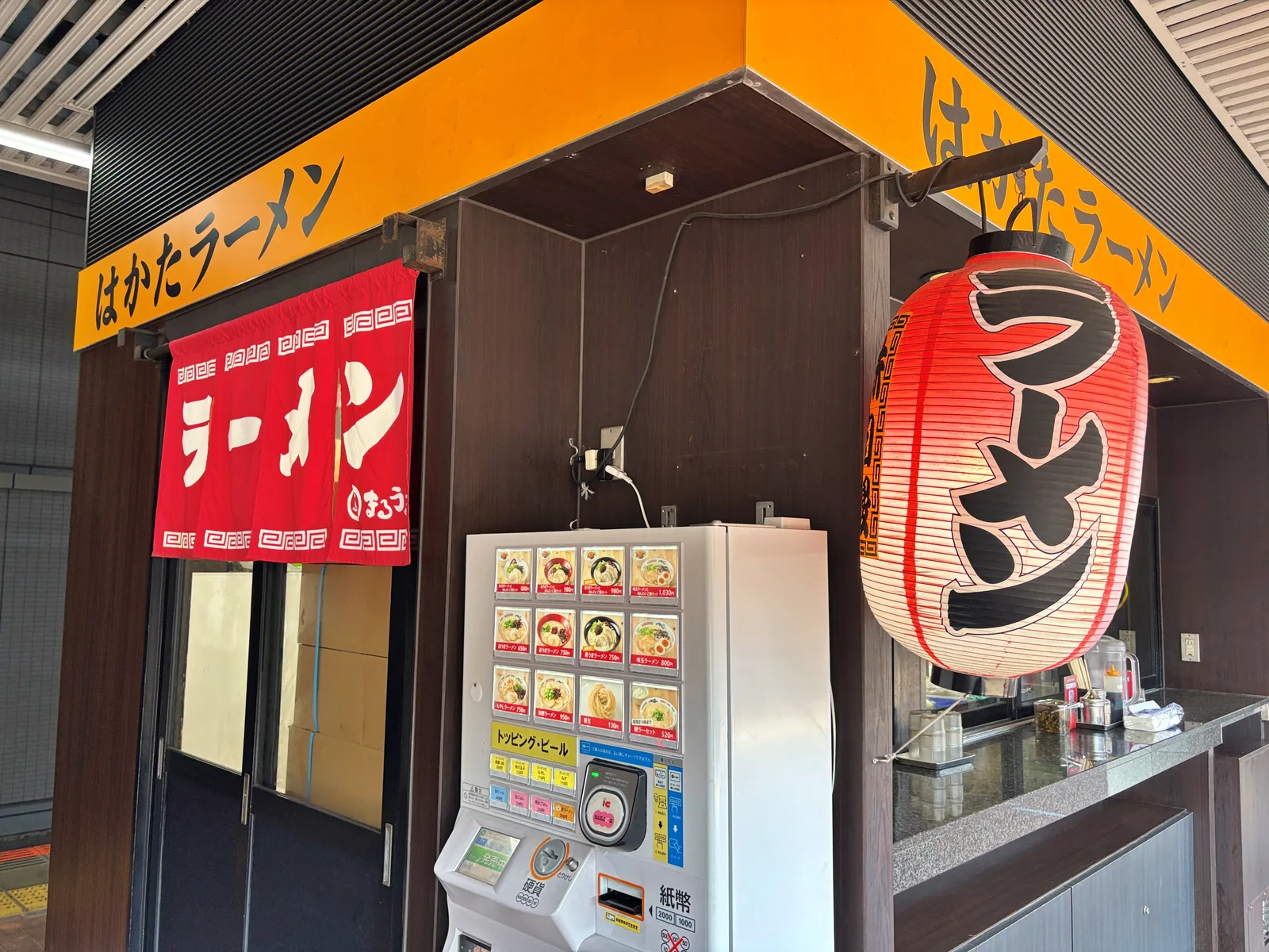 在来線ホームの上にある「はかたラーメン」。赤いのれんに「ラーメン まるうま」、右手に「味自慢 ラーメン」の提灯