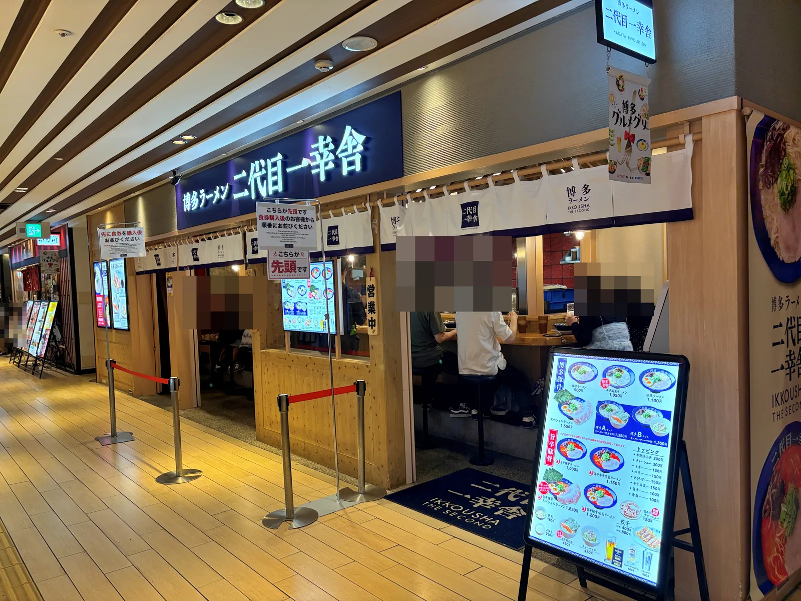 博多1番街の二代目一幸舎。紺の看板と白いのれん。店頭に「こちらが先頭です」の案内とメニュー看板