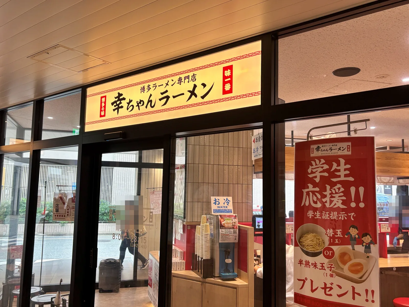 幸ちゃんラーメンの外観（10月1日）。ガラス張りで、赤い椅子のテーブル席とカウンター席が見える。右に「学生応援!!」のポスター