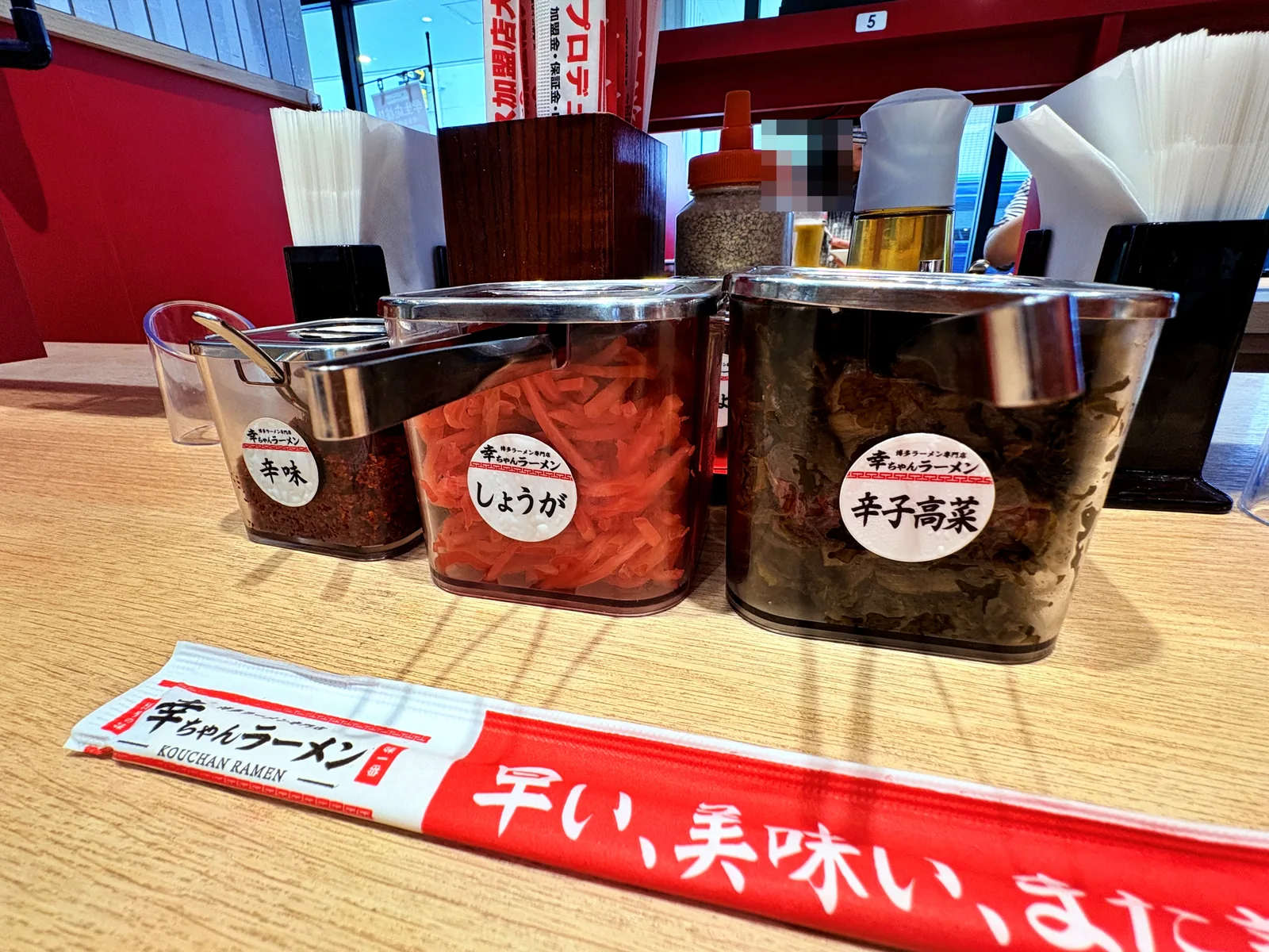 卓上の薬味。辛味・しょうが・辛子高菜。手前の箸袋に「早い、美味い、また来たい」