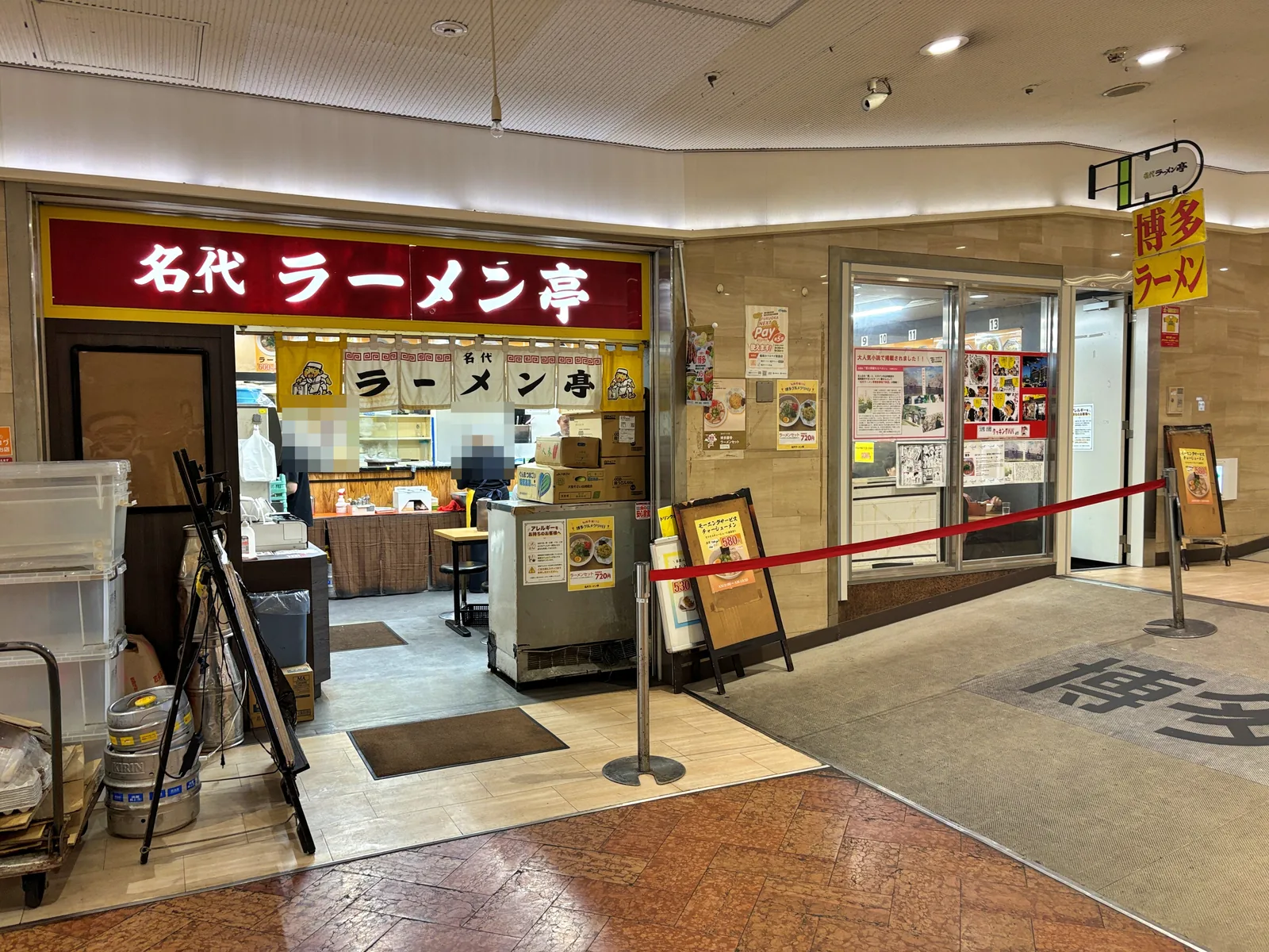 名代ラーメン亭 博多駅地下街店の外観。赤い看板と黄色ののれん。店頭にモーニングサービスの看板