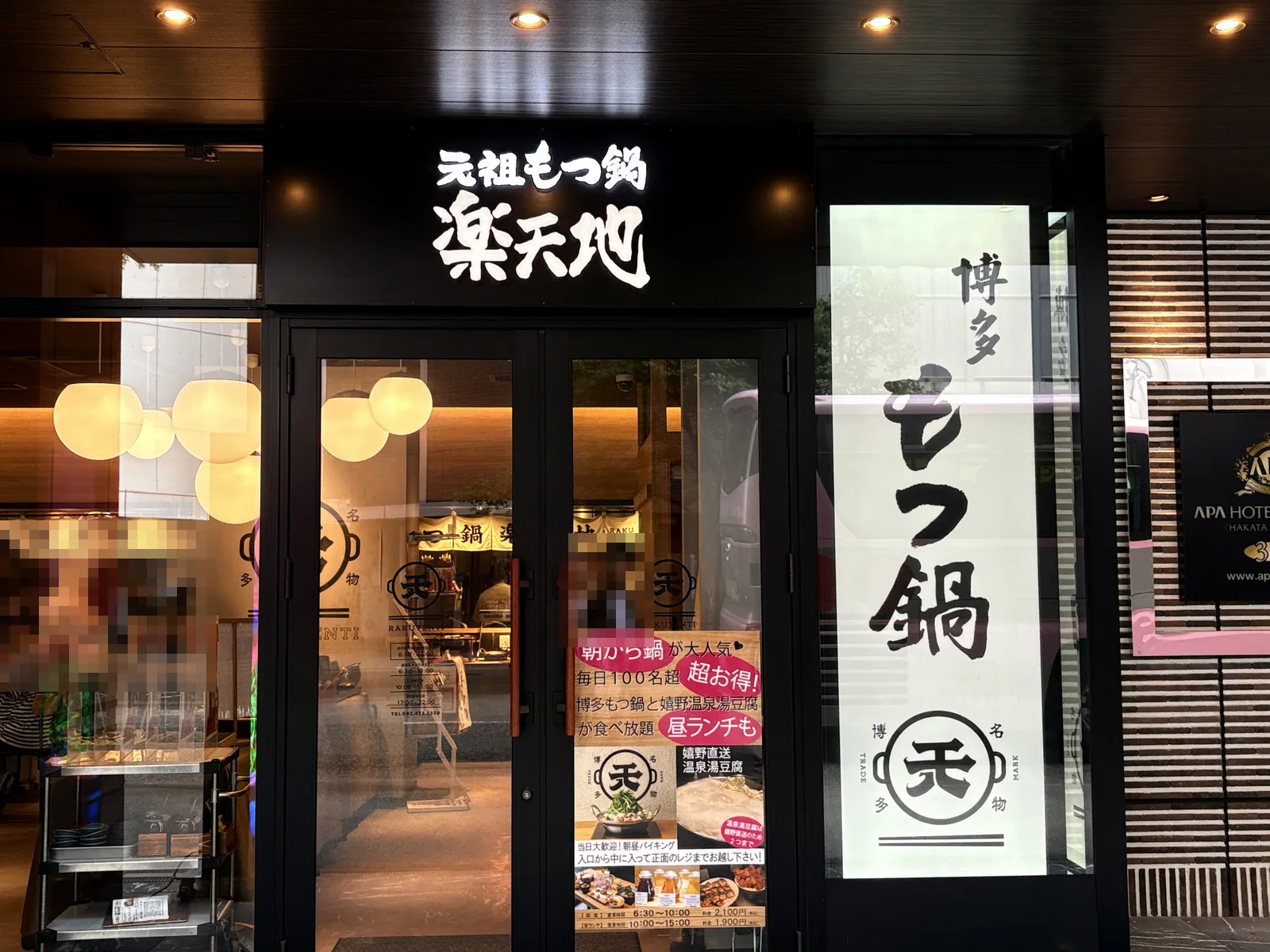 楽天地の入口。看板「元祖もつ鍋 楽天地」、右に「博多 もつ鍋」の大きな行灯、扉に朝食のポスター
