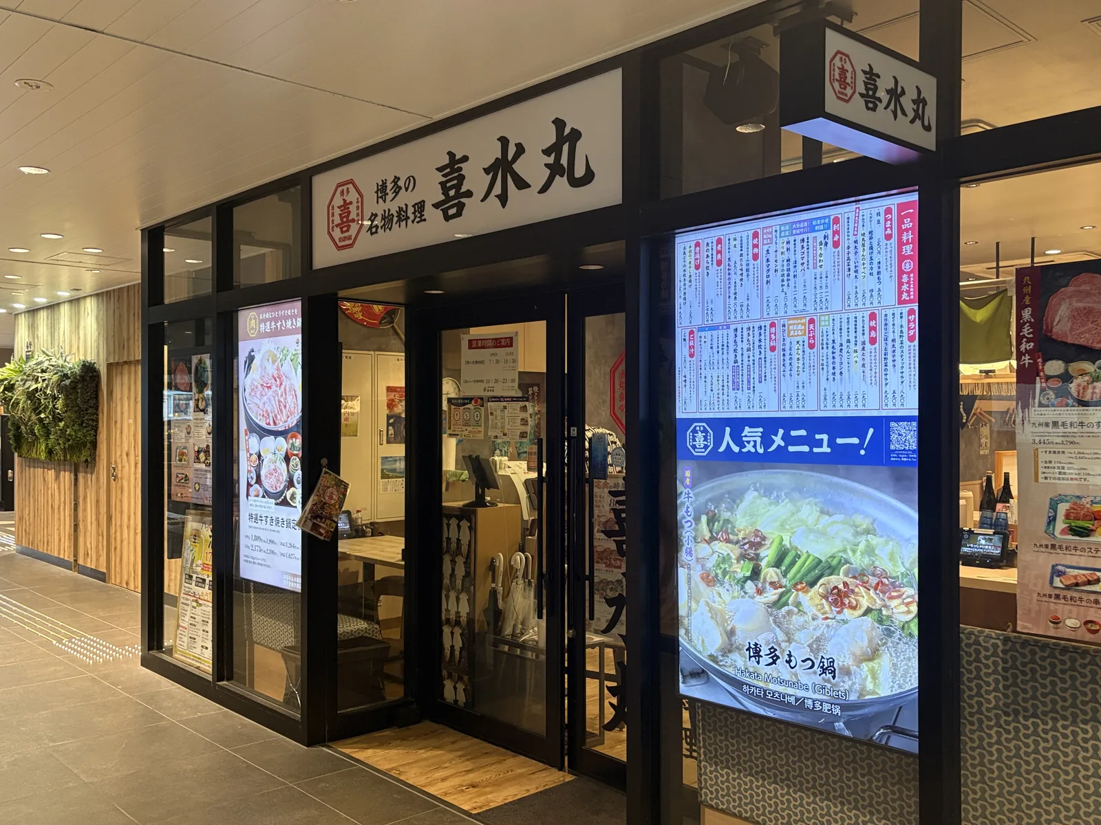 喜水丸 博多デイトスアネックス店(6:44)。看板「博多の名物料理 喜水丸」、右に「人気メニュー!博多もつ鍋」の大型画面