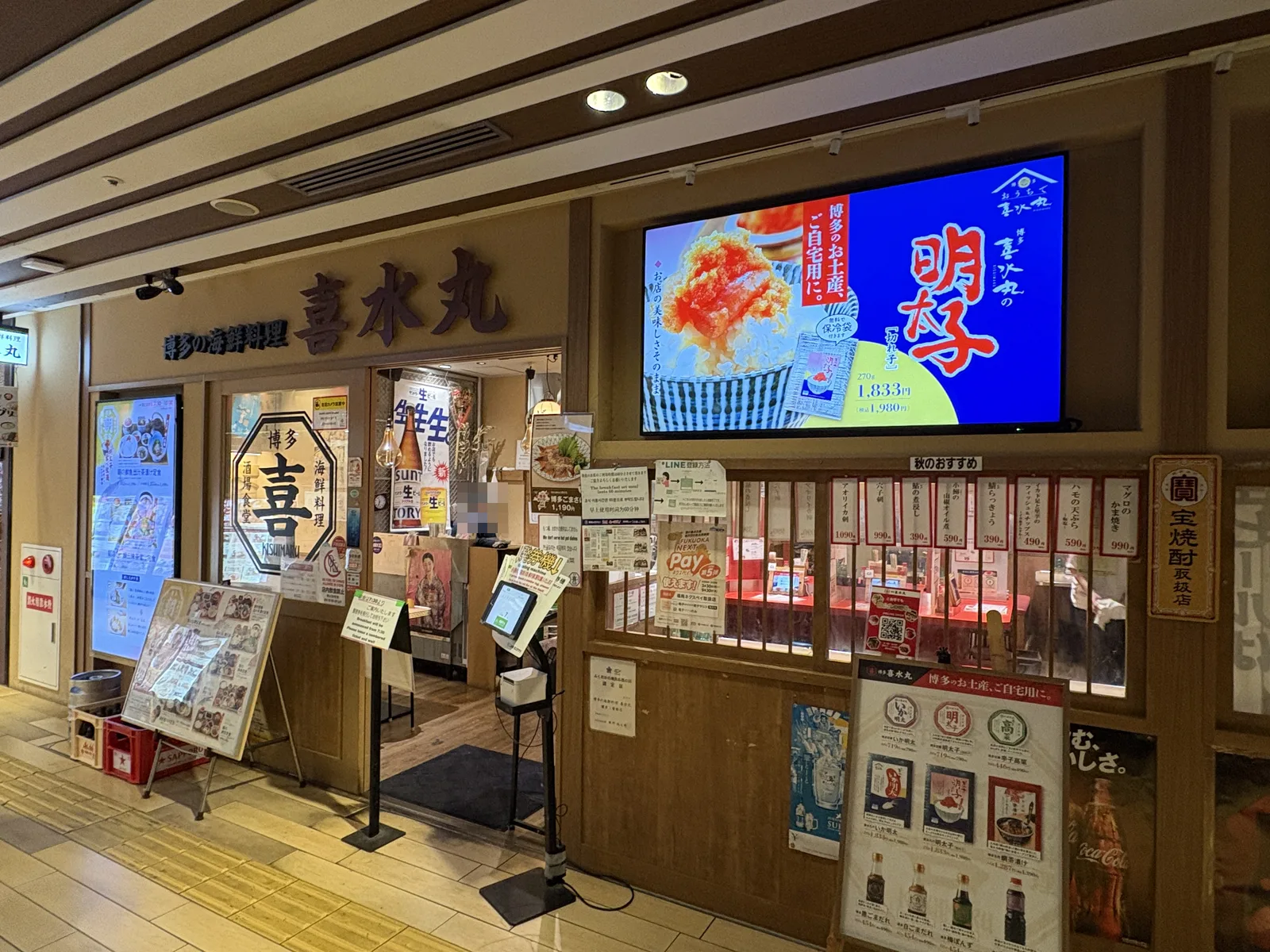 喜水丸 博多1番街店(6:59)。看板「博多の海鮮料理 喜水丸」、右上に明太子の大型画面