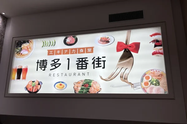 博多1番街の看板。「エキナカ食堂 博多1番街 RESTAURANT」の文字と、もつ鍋・ラーメン・寿司などの料理写真
