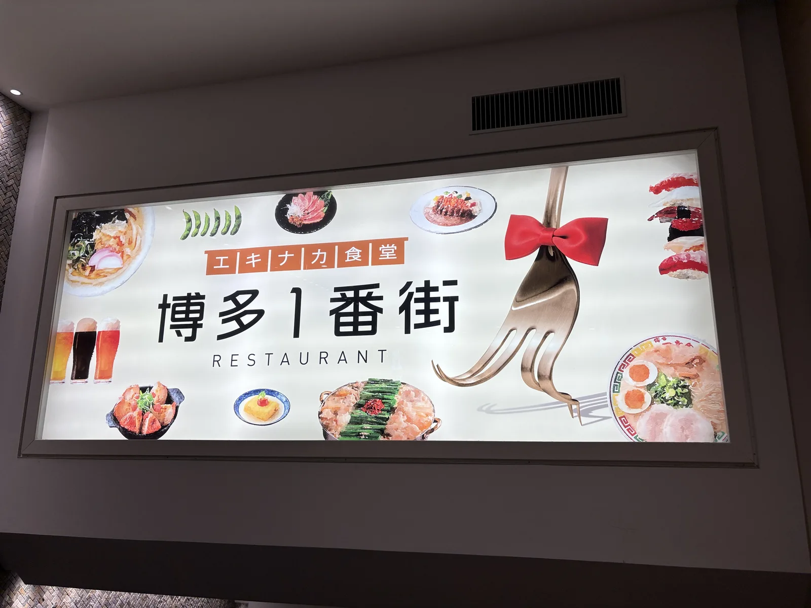 博多1番街の看板。「エキナカ食堂 博多1番街 RESTAURANT」の文字と、もつ鍋・ラーメン・寿司などの料理写真