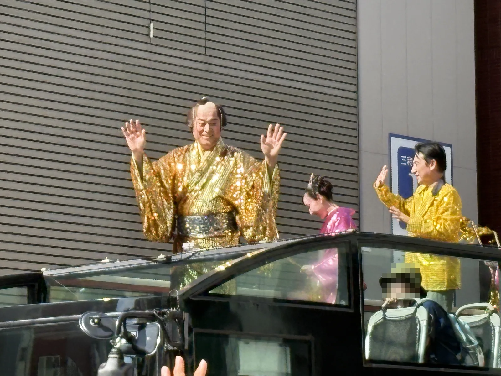 オープンカーの上で、金色の衣装の松平健さんが両手を振る。後ろにも金色・ピンクの衣装の出演者