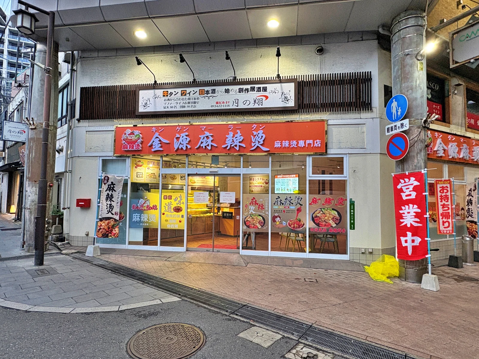 通りの角から見た金源麻辣湯。2階の居酒屋の看板の下に、オレンジの看板とガラス張りの入口