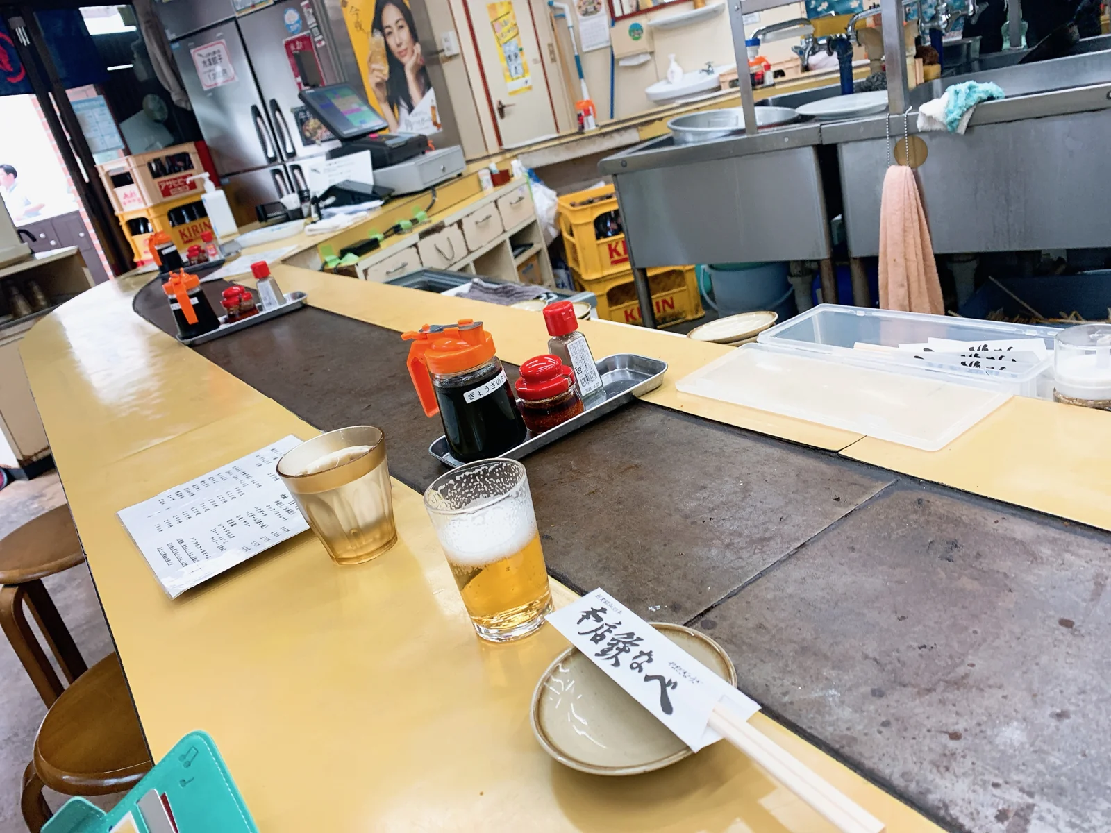 本店鉄なべ 黒崎本店の店内。鉄板を囲むカウンター席に、餃子のたれと調味料、生ビール、箸袋が並ぶ