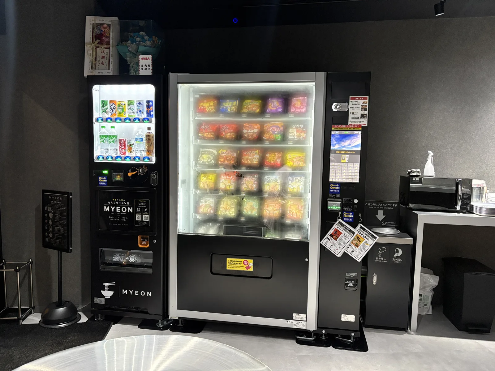 自販機の全景。左にドリンクの自販機、右にラーメンの自販機。壁はグレー