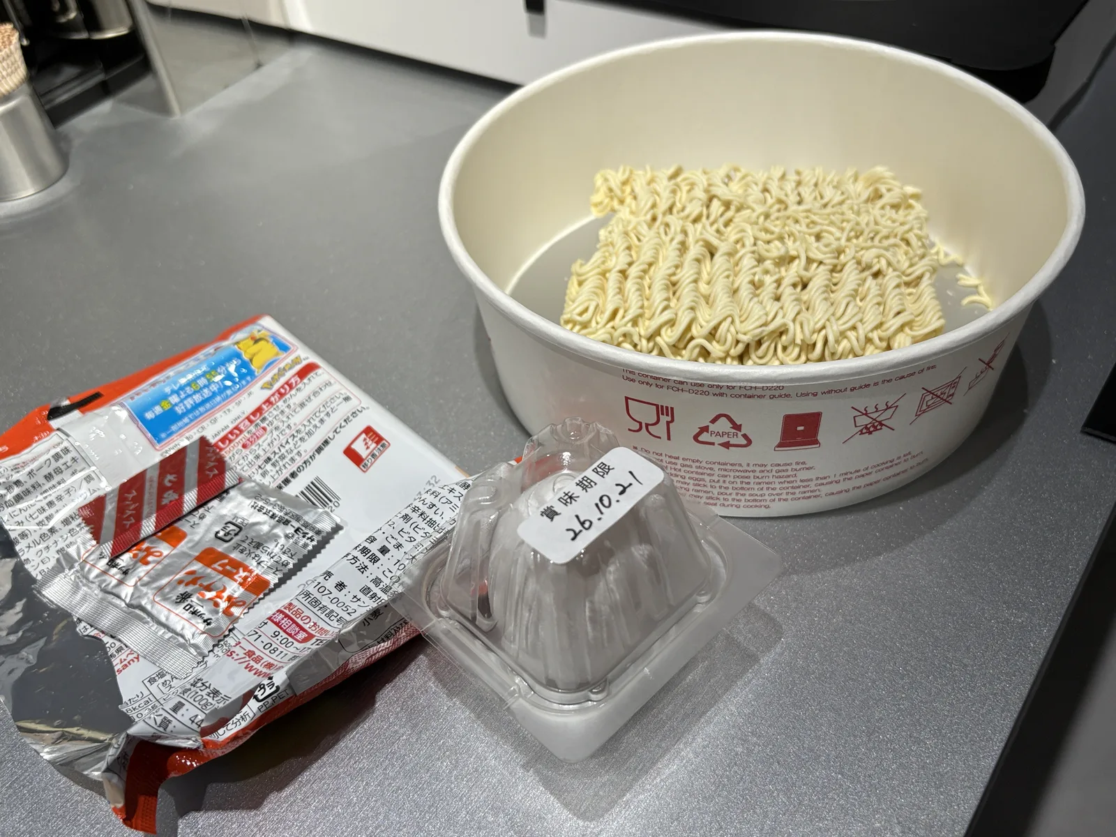 白い紙の専用容器に袋麺を入れたところ。横にサッポロ一番の袋とパック入りのたまご