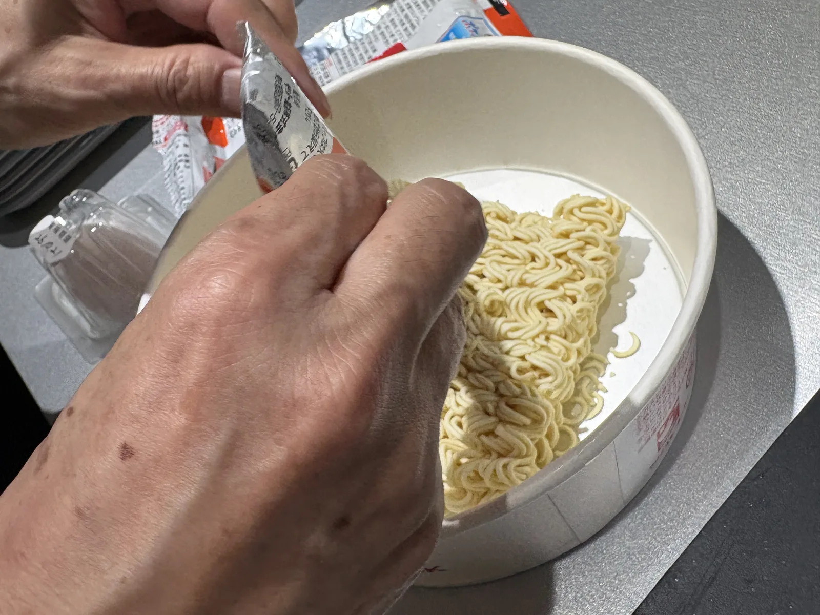 手で粉末スープの袋を破り、麺の上に入れている