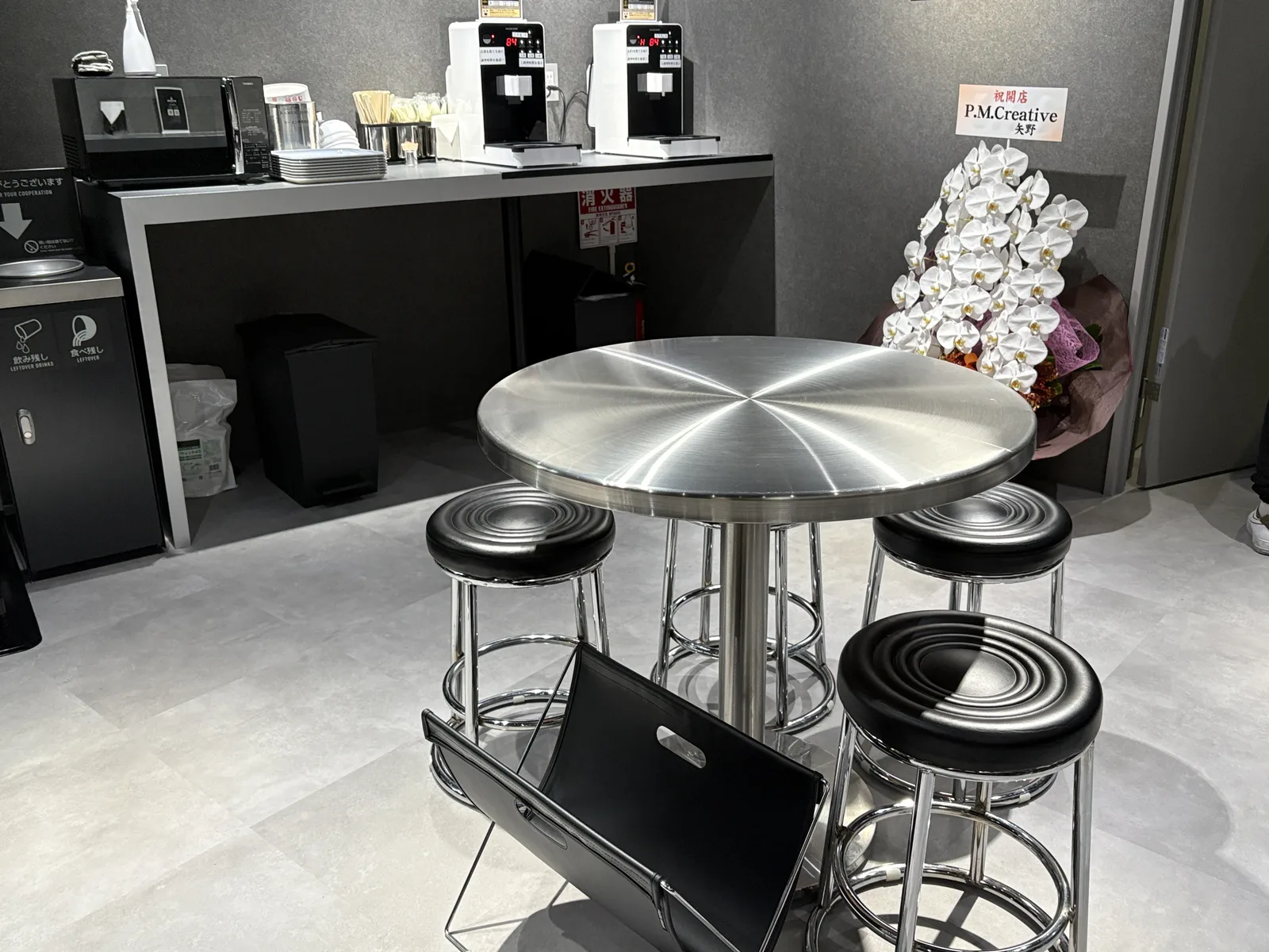 調理コーナー。自動調理器が2台並び、横に電子レンジと紙ボウル。手前にテーブル席