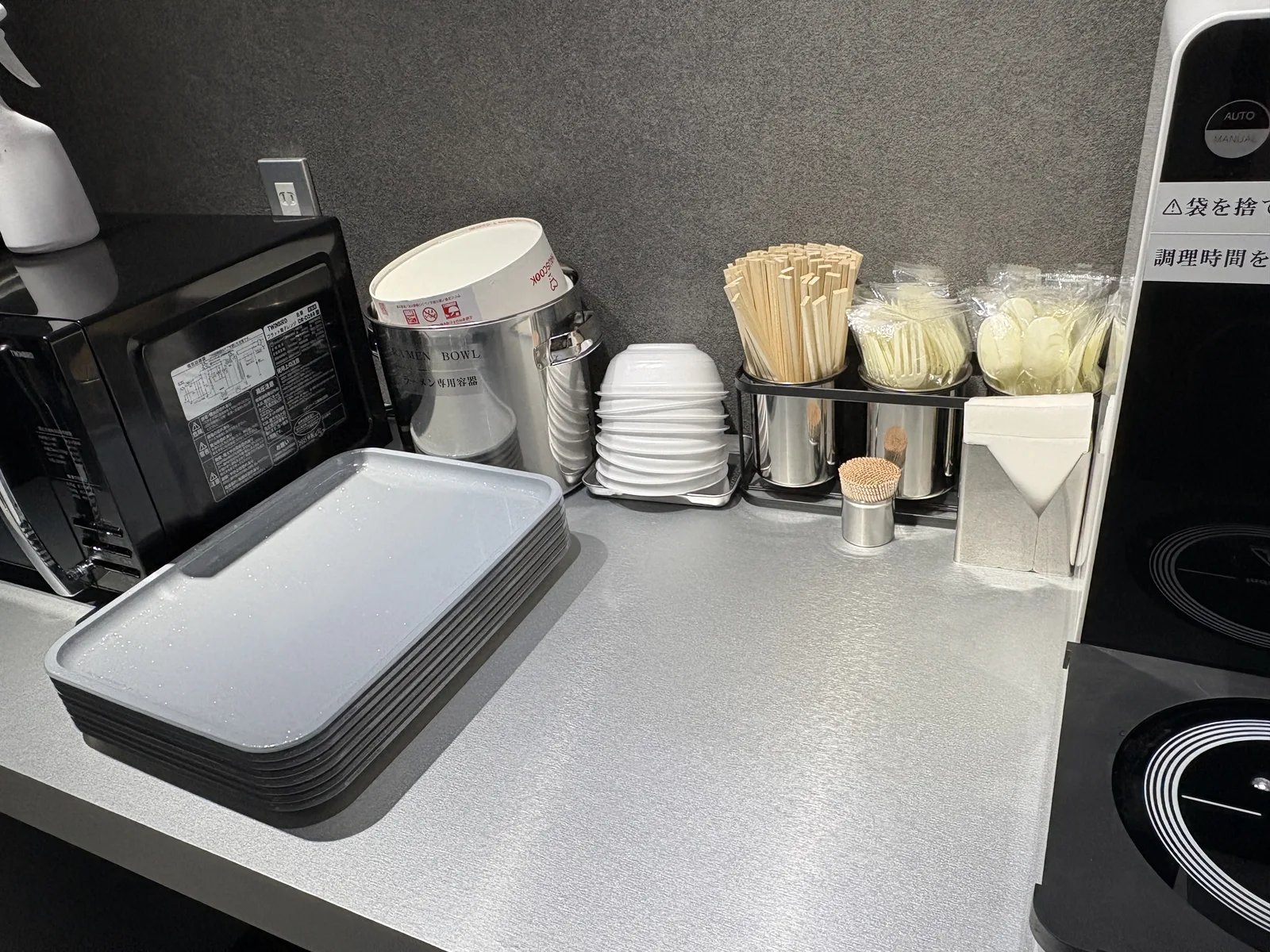 専用容器、紙ボウル、グレーのトレー、割り箸、電子レンジが並ぶ