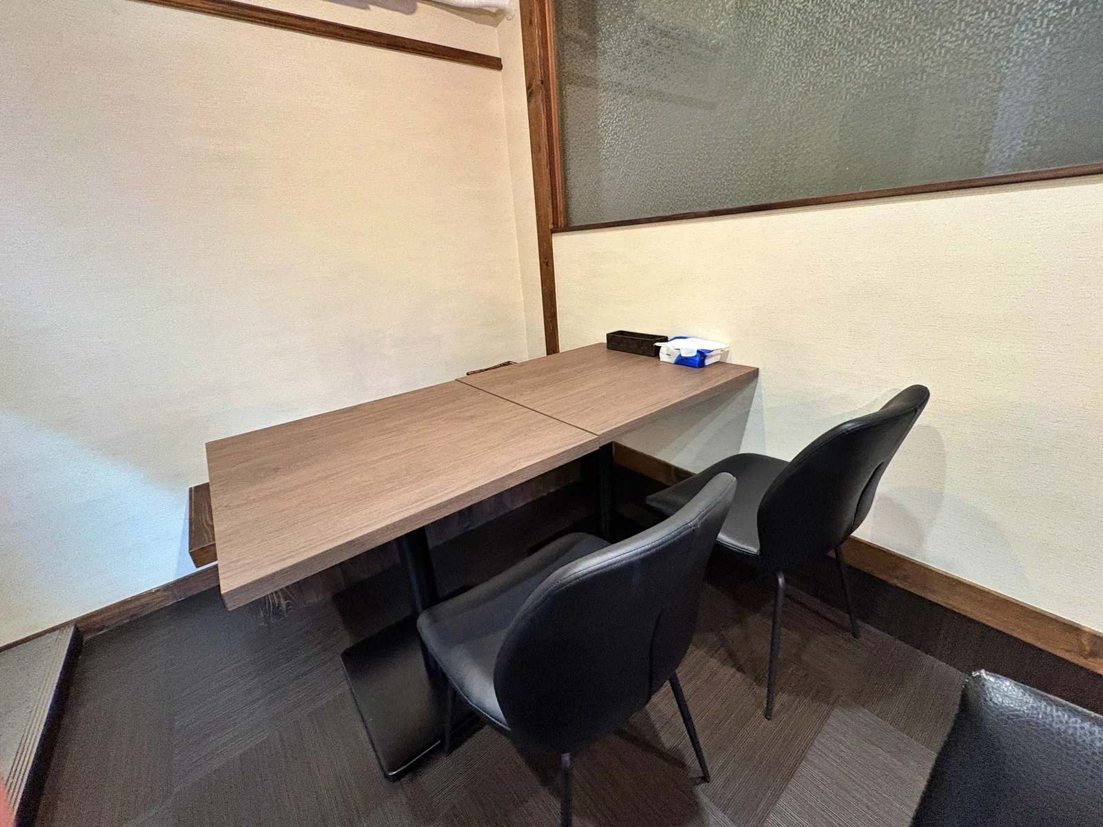 壁際の4人掛けテーブル席。木目のテーブルに黒い椅子