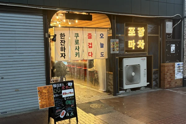 麻生ビル1階の韓国屋台ポチャの店頭。ハングルののれんが4枚下がり、手前に「韓国屋台ポチャ」の黒板が立つ