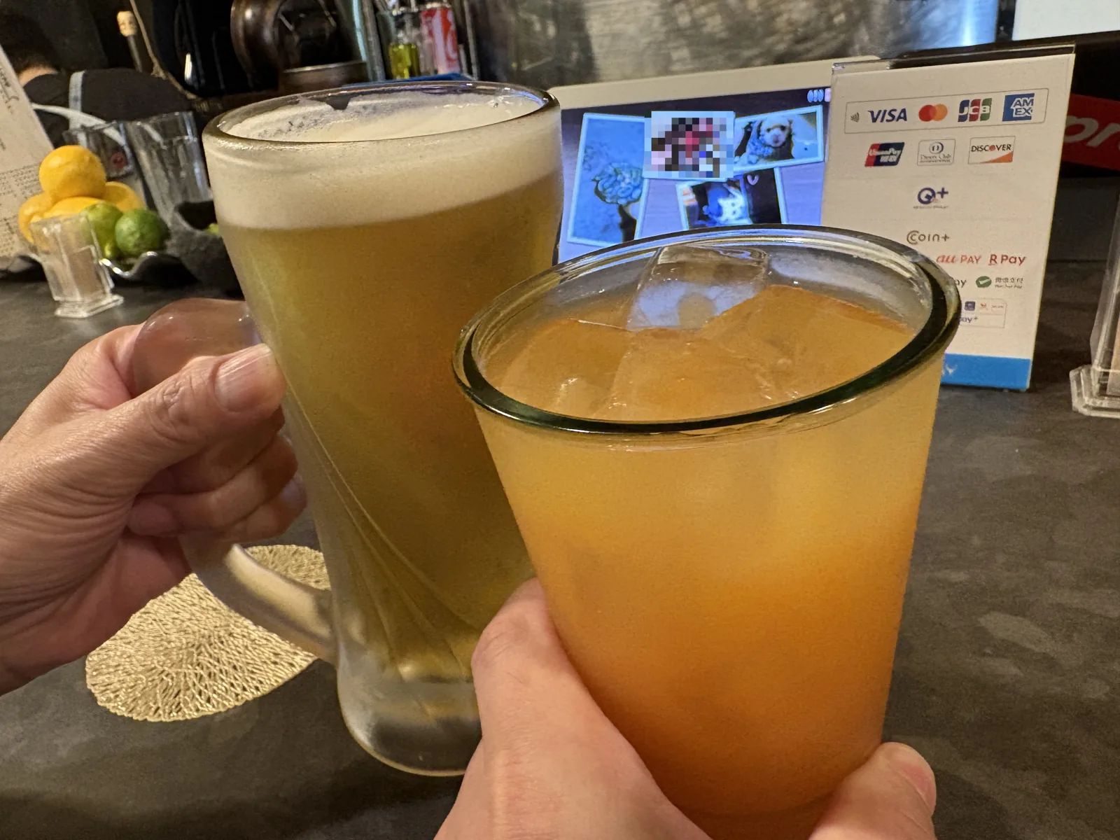 ジョッキの生ビールと、氷の入ったオレンジ色のドリンクで乾杯。奥にキャッシュレス決済の案内