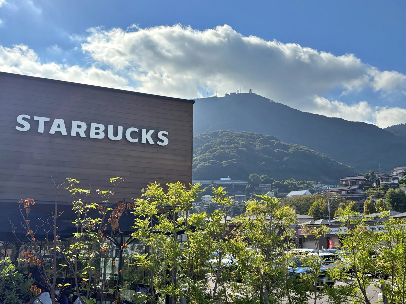 STARBUCKSの文字の外壁と、背後にそびえる皿倉山