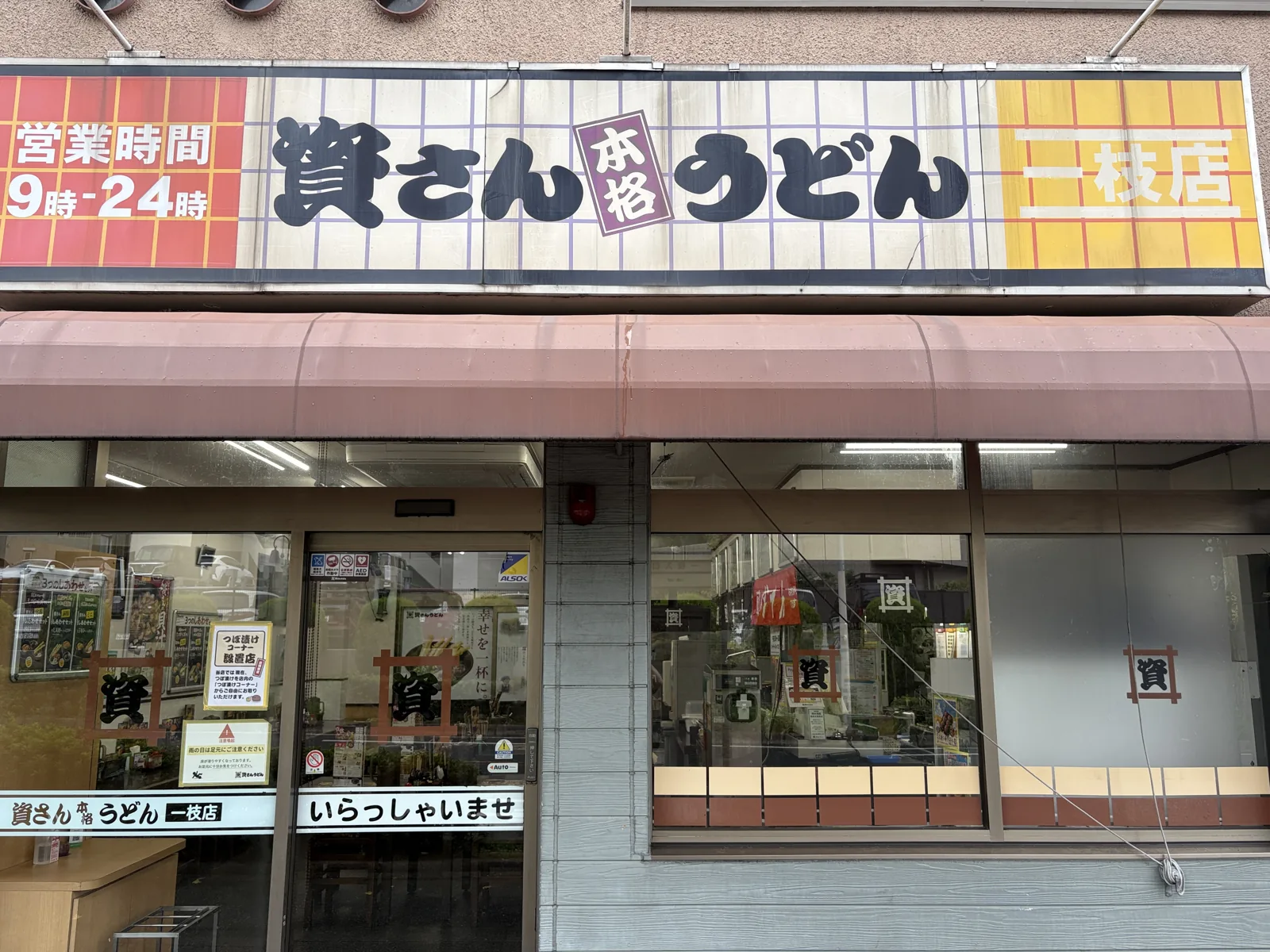 看板「資さん本格うどん 一枝店」。左に「営業時間 9時-24時」
