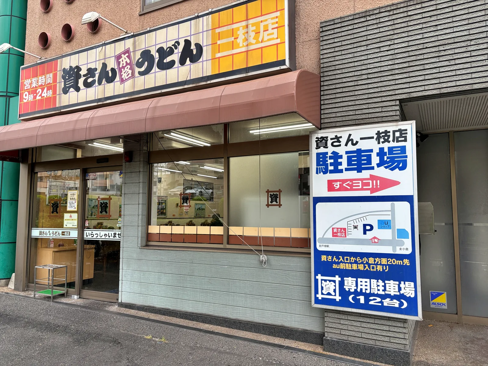 資さんうどん一枝店の外観。看板に「営業時間 9時-24時」、右に「専用駐車場(12台)」の看板