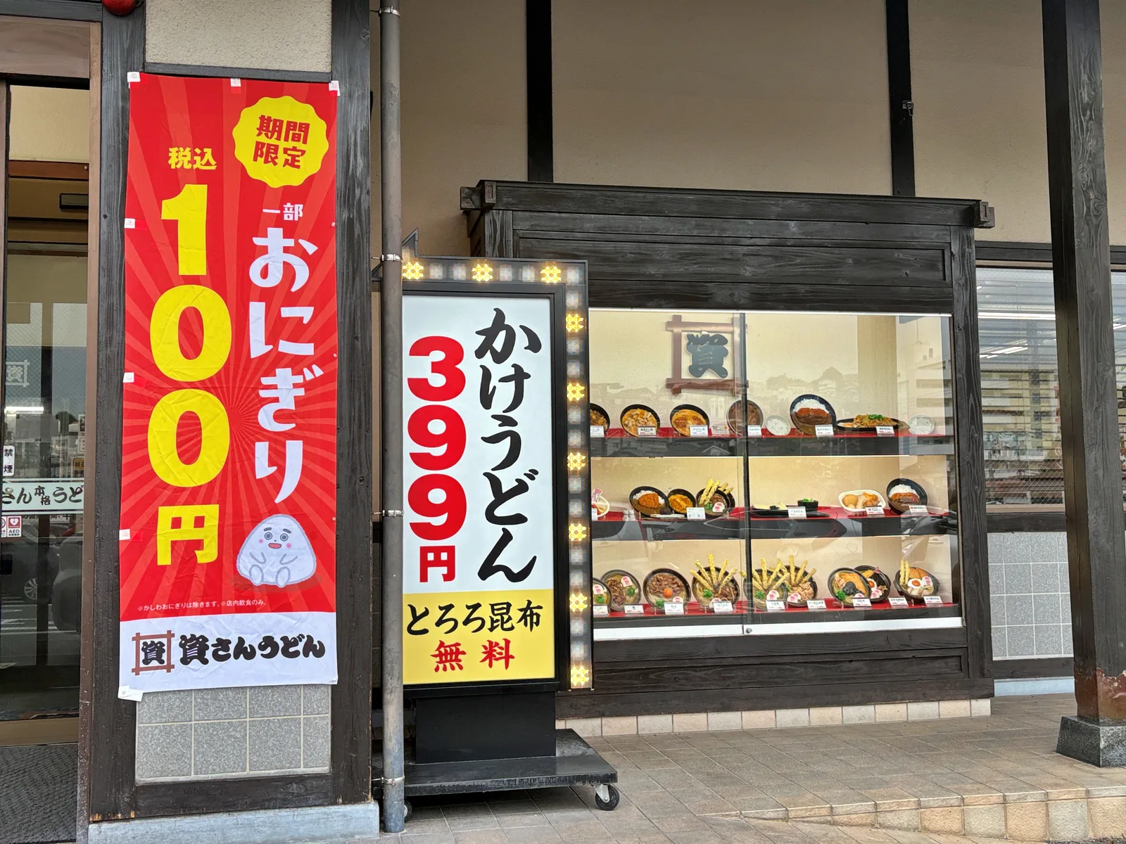 資さんうどん鞘ヶ谷店の店頭。LEDで縁取られた電飾看板「かけうどん 399円 とろろ昆布無料」と、のぼり「期間限定 一部おにぎり 税込100円」