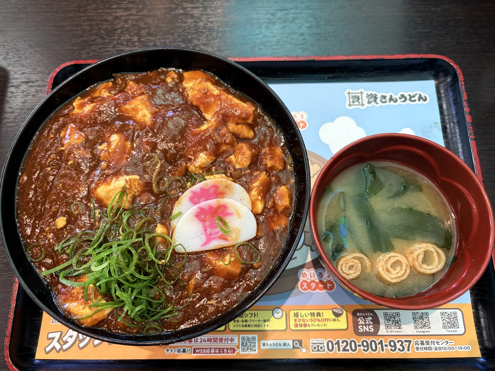 トレーに麻婆丼とみそ汁。麻婆豆腐が丼いっぱいに広がり、刻みネギと「資」のかまぼこがのる