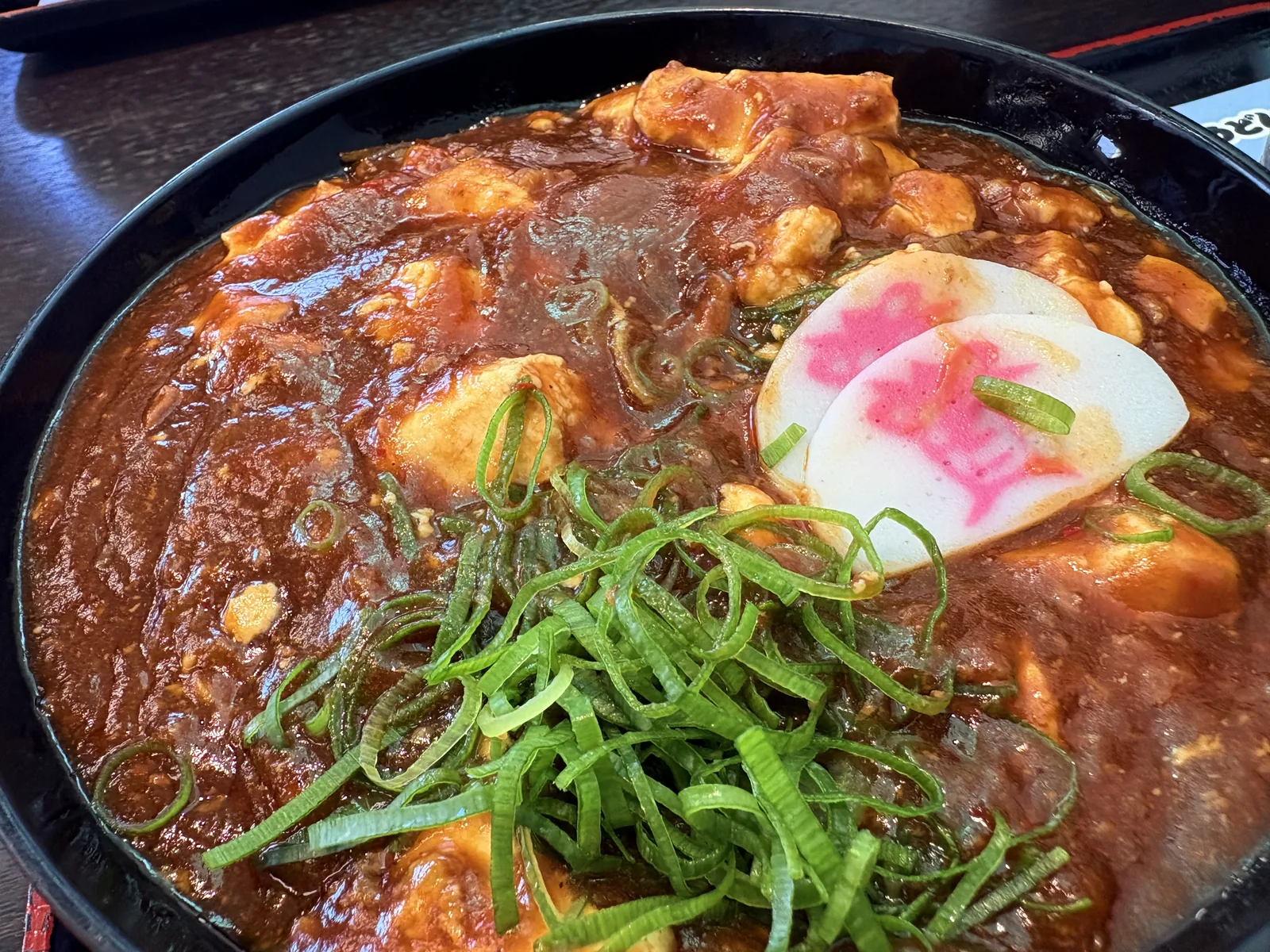 麻婆丼のアップ。大きな角切りの豆腐、山盛りの刻みネギ、「資」の字のかまぼこ2枚