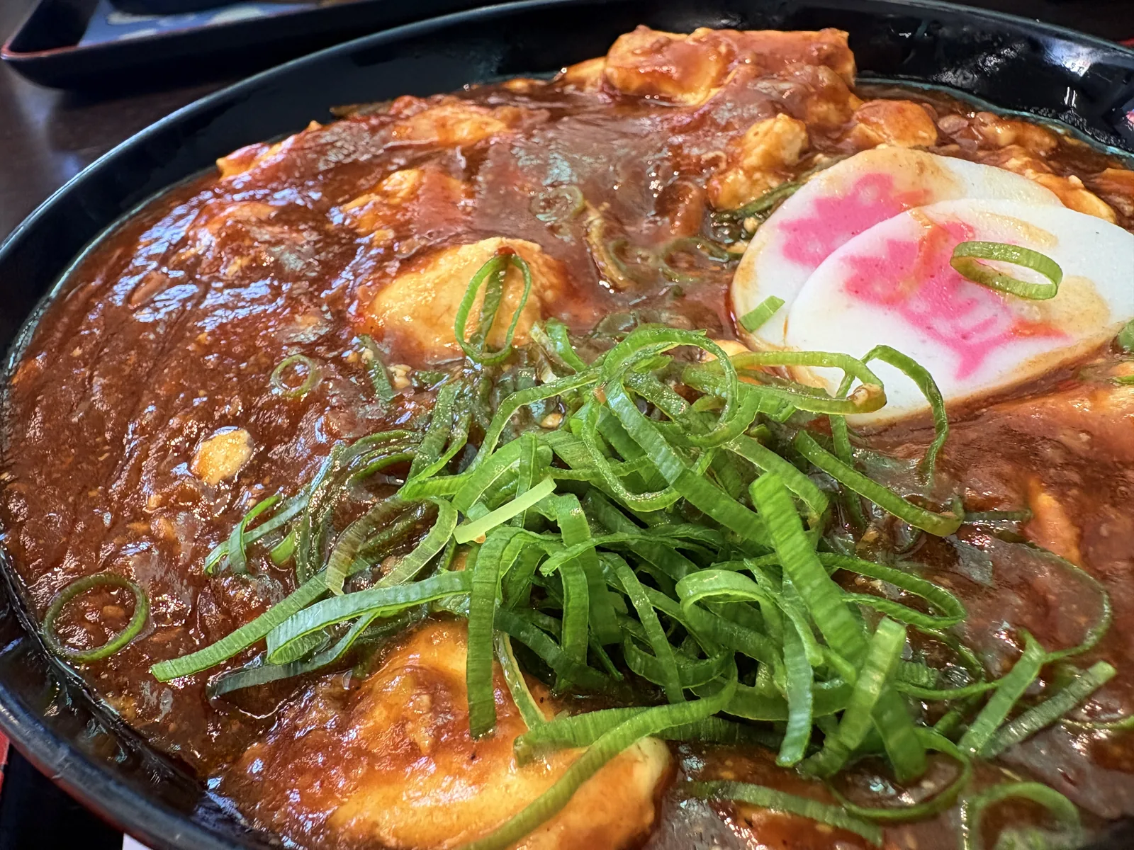 麻婆丼のアップ。麻婆のあんがテリテリに光り、刻みネギと「資」のかまぼこがのる