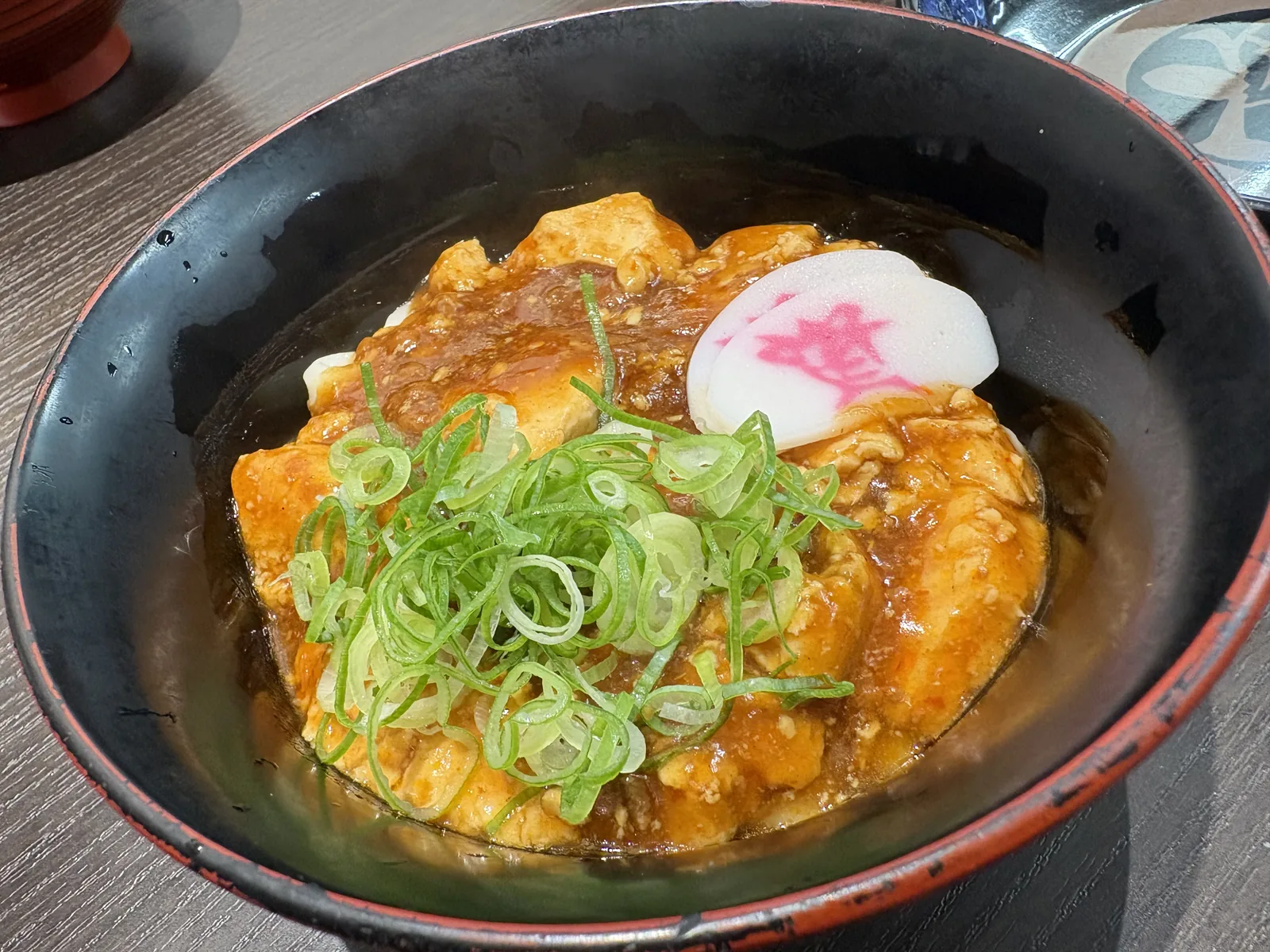 資フェスVol.2で出た試作の麻婆うどん。黒い丼に麻婆豆腐、刻みネギ、資ぼこ