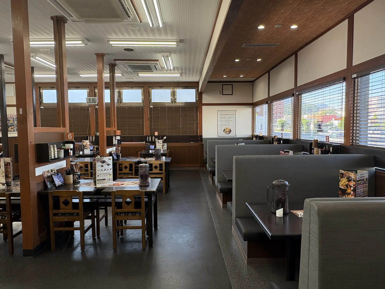 鞘ヶ谷店の店内。左に木の椅子のテーブル席、右の窓際にグレーのボックス席。窓にはブラインド